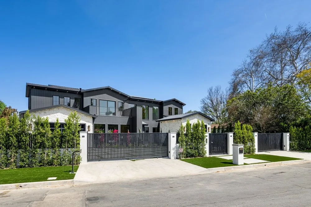 Black metal driveway gate and fence in front of a modern home