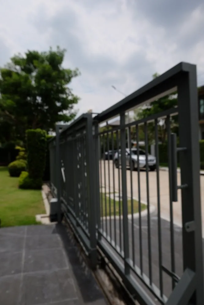 Close-up of a black steel picket gate along a driveway