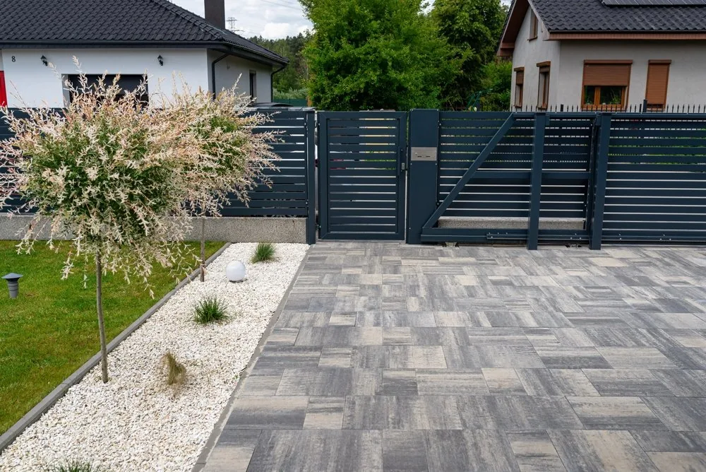 Dark horizontal-slat swing gate and matching fence across a paver driveway