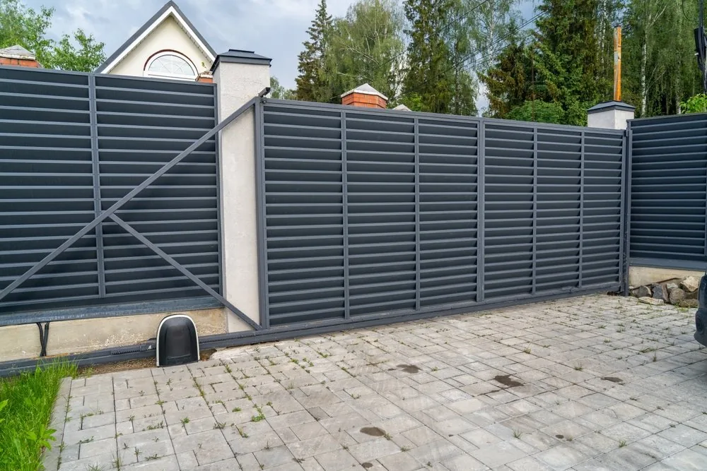 Gray louvered sliding gate with its opener motor at the base