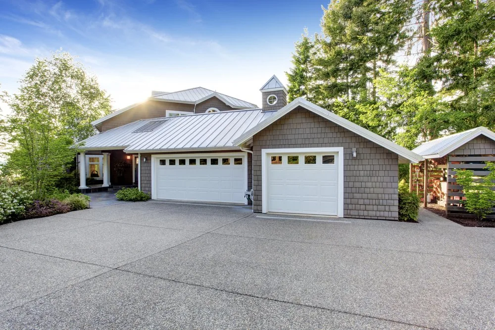 Two single white garage doors with window tops on a shingle-sided house