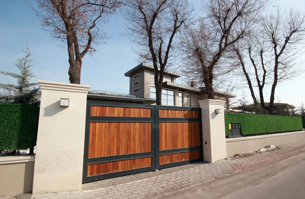 Horizontal wood-slat driveway gate in a dark steel frame between stucco pillars